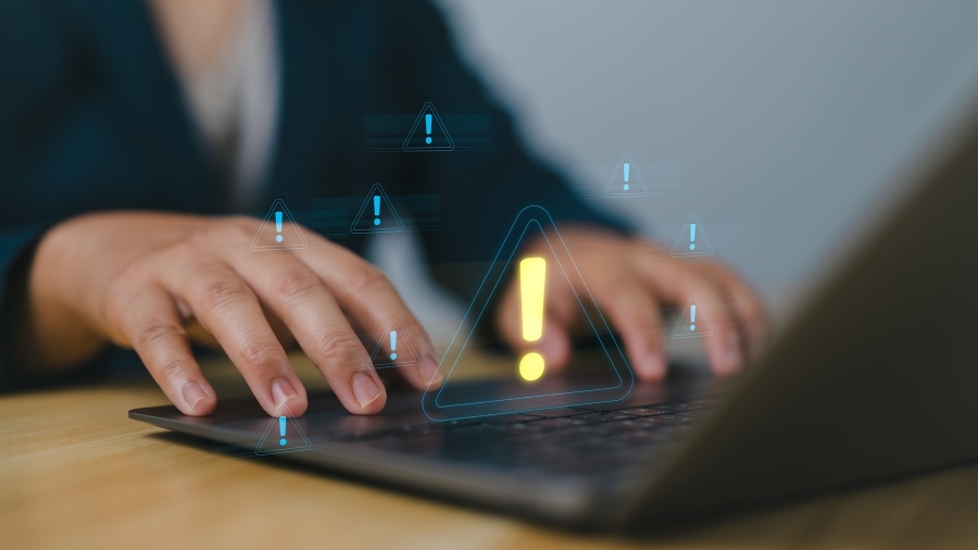 Somebody typing on a laptop keyboard, with a yellow exclamation point floating over their hands.